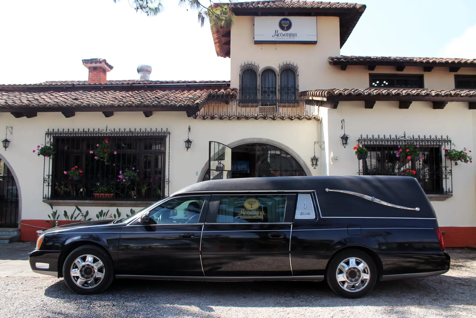 Carroza fúnebre negra de Hosanna estacionada frente a la casa de velación