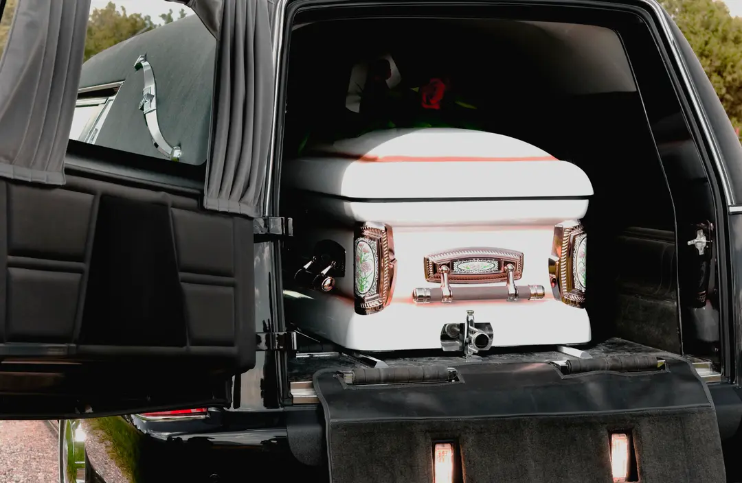 Carroza fúnebre negra con la puerta trasera abierta y un ataúd blanco dentro