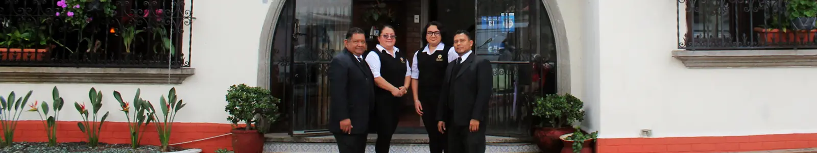Cuatro integrantes del equipo de Hosanna, de traje oscuro, en la puerta de arco de la casa